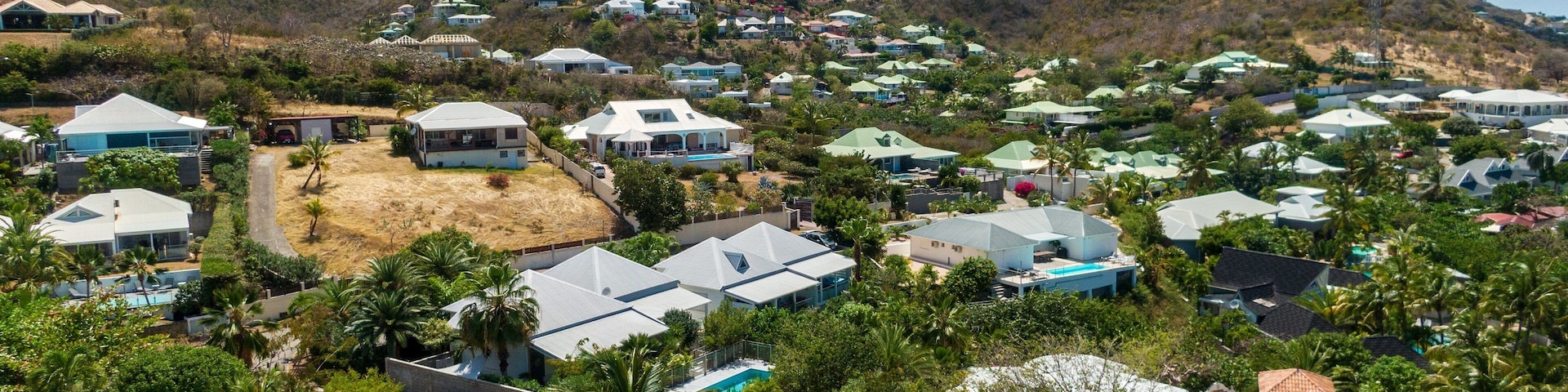 A hillside residential area with houses, a swimming pool, and mountains in the background.