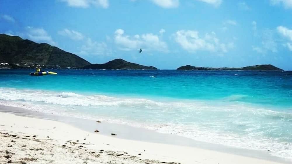 Ein Strand mit klarem türkisblauem Wasser, weißem Sand und vorgelagerten Inseln.