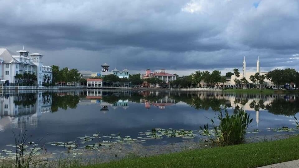 A calm lake with reflections of buildings and a cloudy sky.