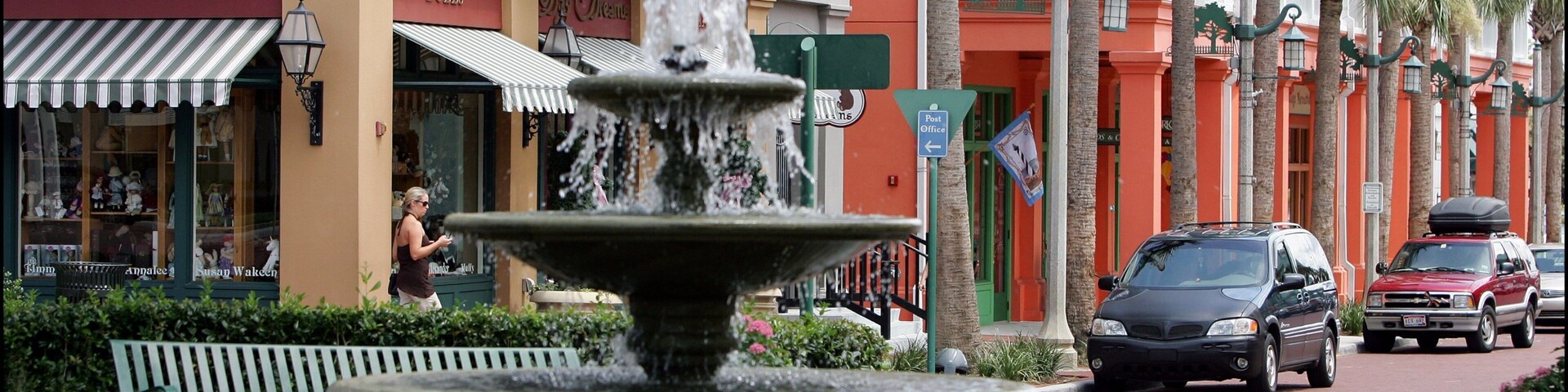 Una fuente en una plaza con tiendas y palmeras.