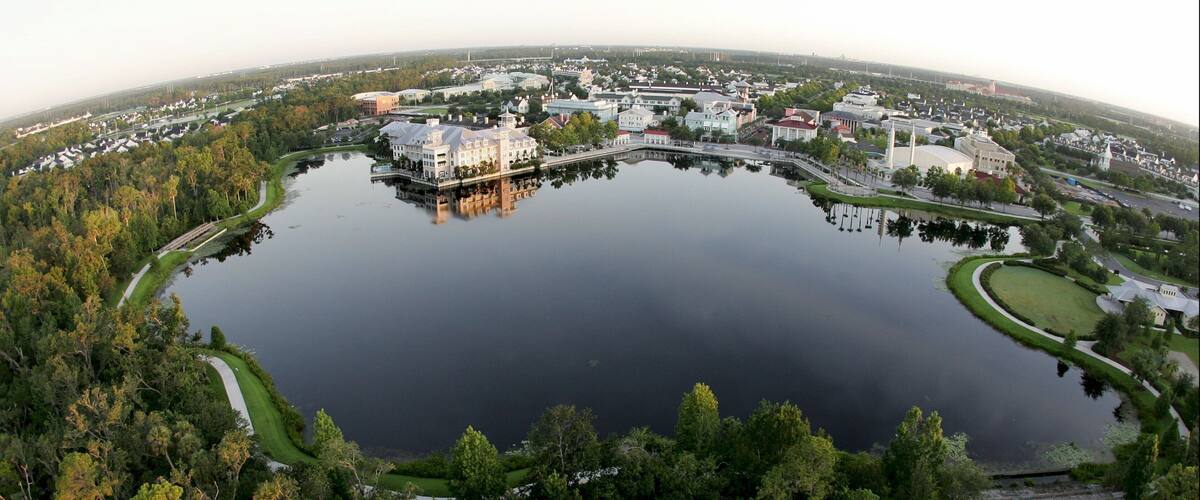 A large lake surrounded by dense forest and a mix of residential and commercial buildings.