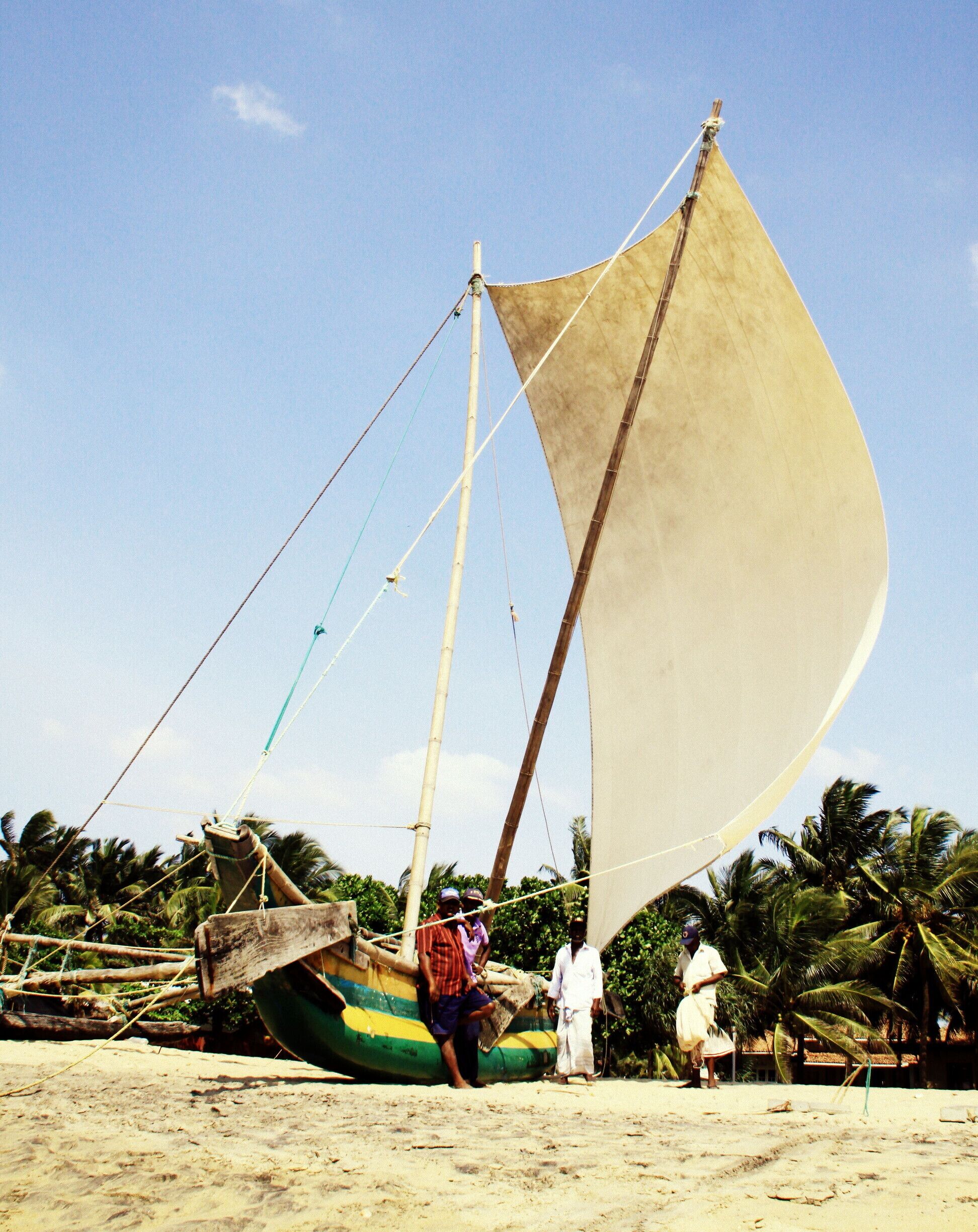 A traditional sailboat on a sandy beach with palm trees in the background.