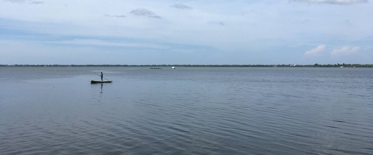 A calm body of water with a person paddling a small boat.