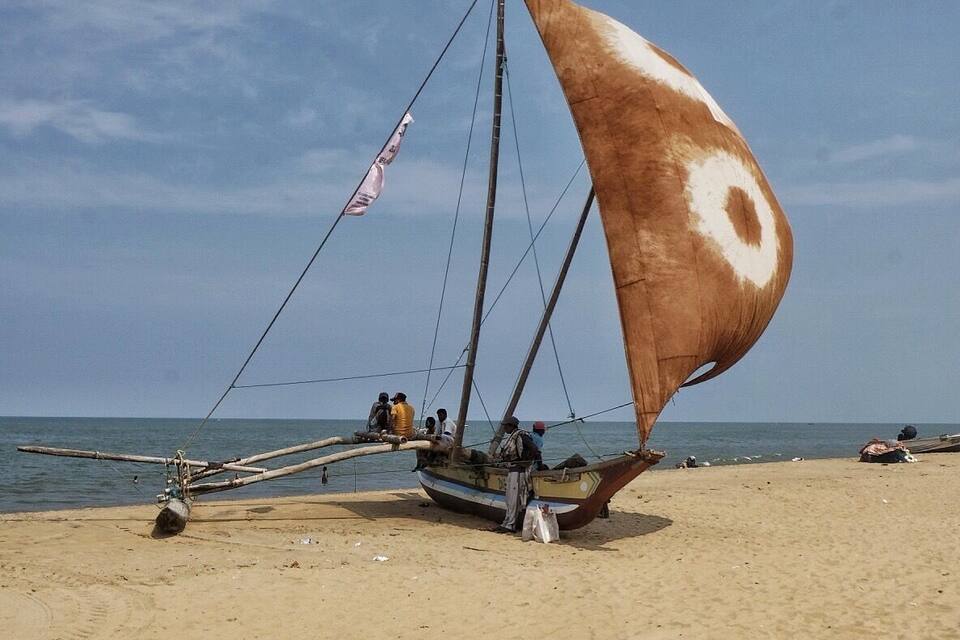 A traditional sailboat with a large sail on a sandy beach.