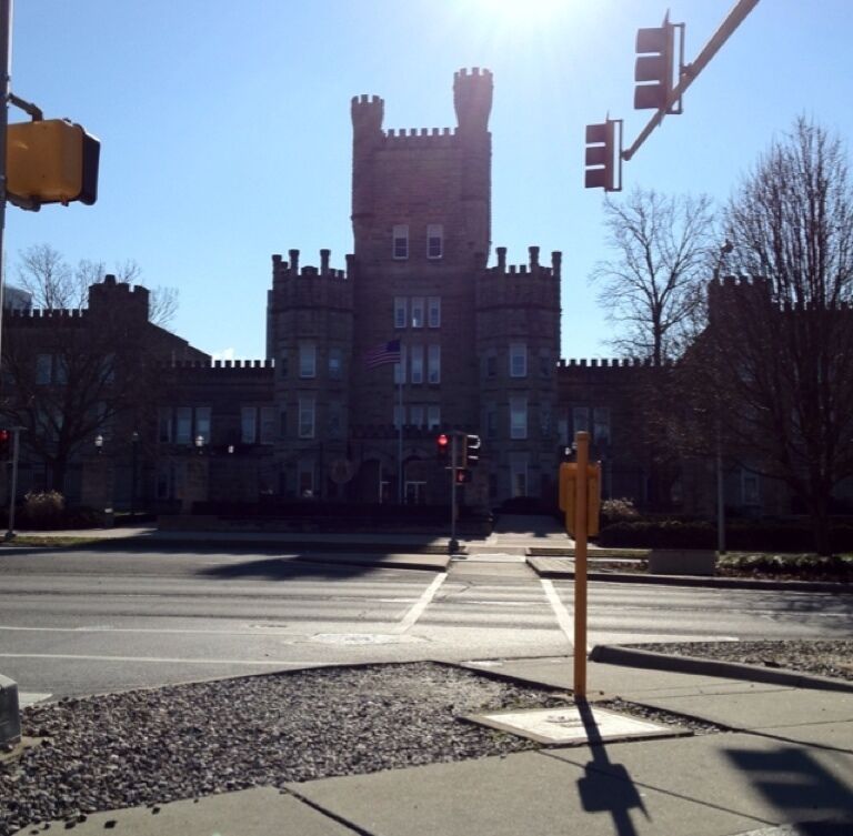A castle-like building with a tall tower, traffic lights, and a crosswalk.
