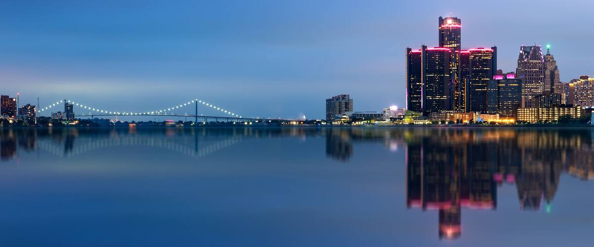 A city skyline with illuminated buildings and a bridge reflected in the water.