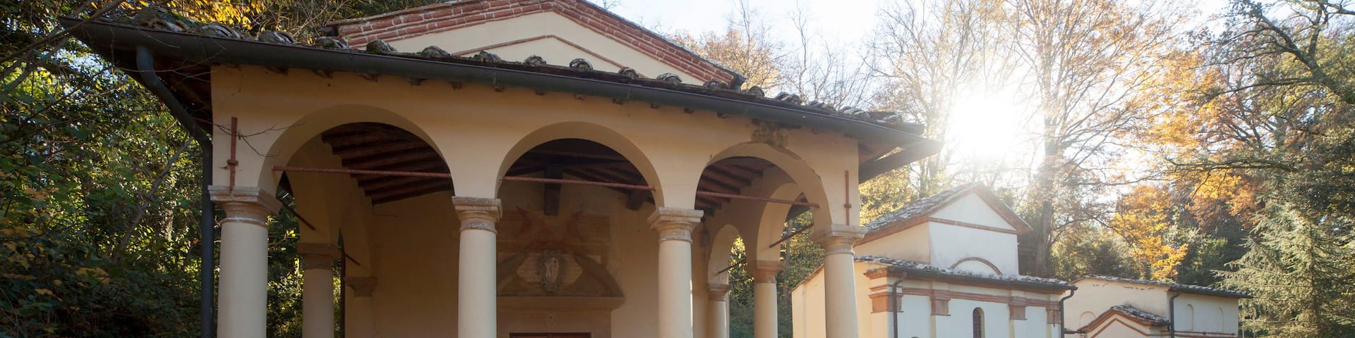 A historical building with a covered porch, columns, and a bell tower, surrounded by trees and a grassy area.