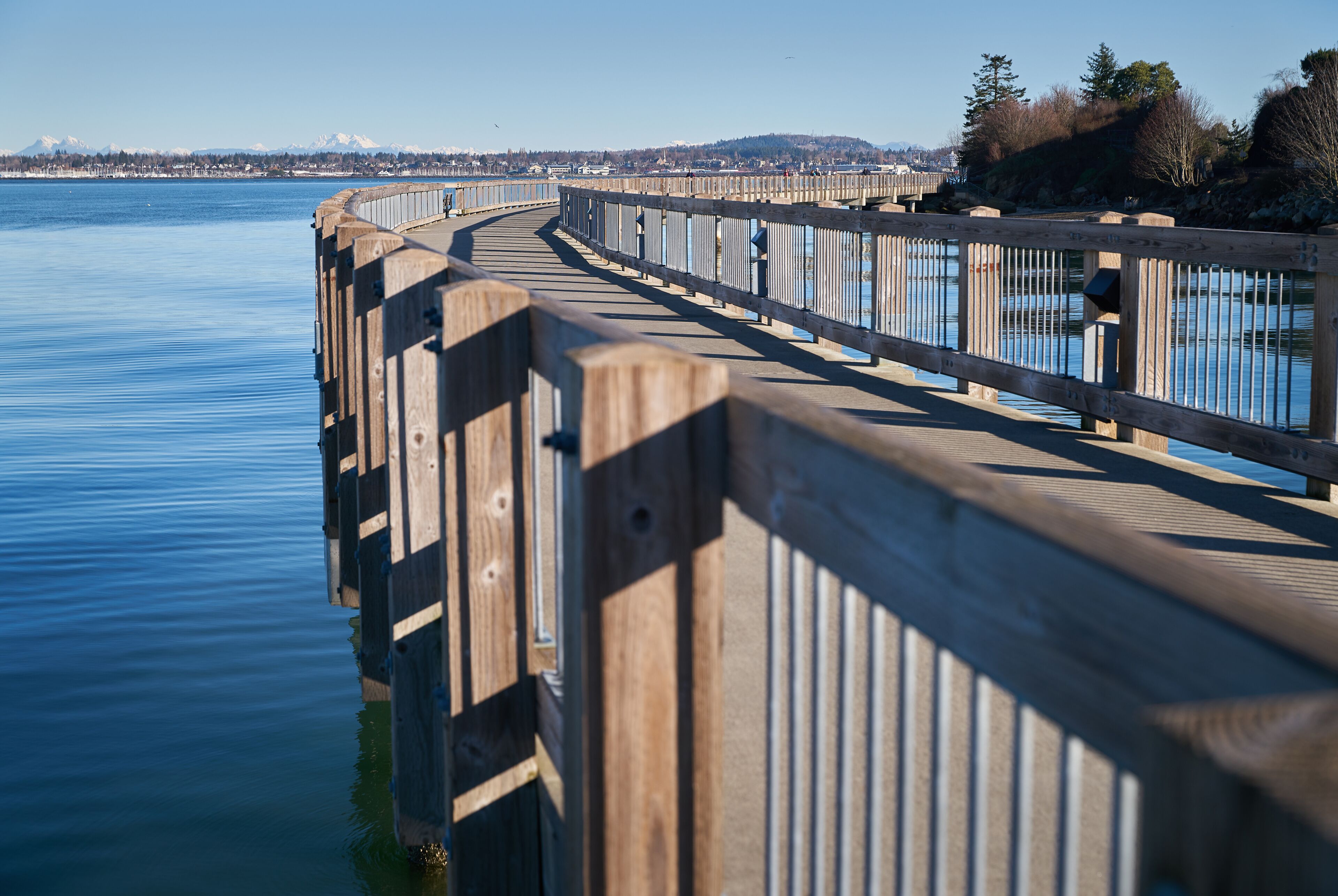 A wooden boardwalk extending over calm water, with a distant mountain range and clear sky.