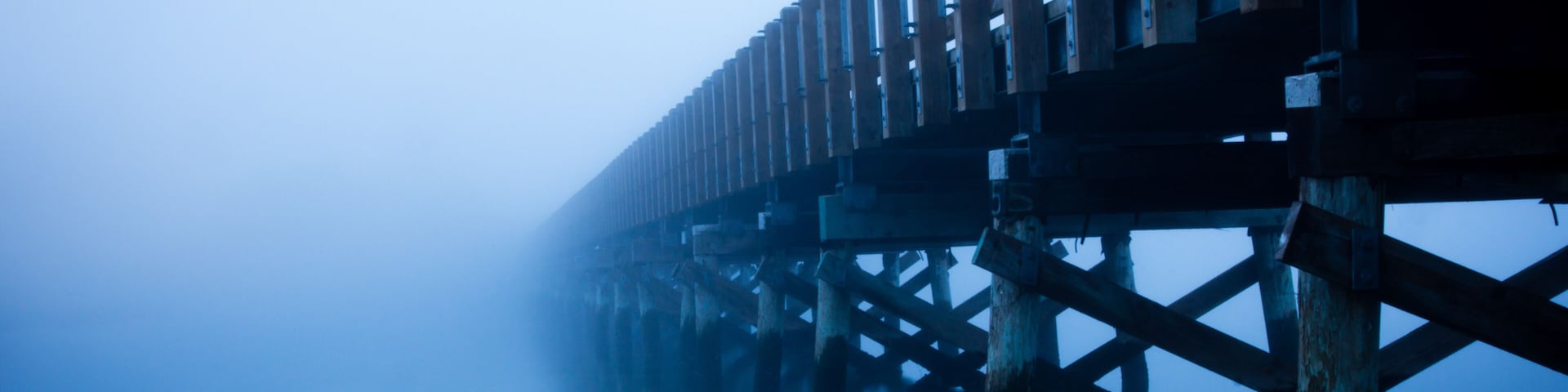 Un muelle brumoso con barandas de madera y un ambiente neblinoso.