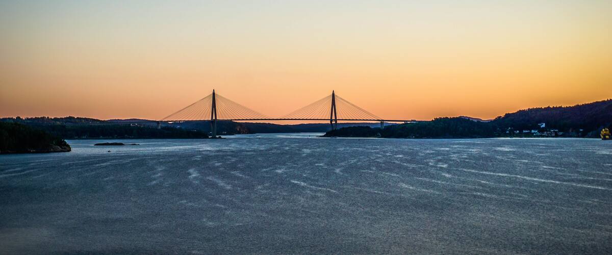 A suspension bridge at sunset with a calm river in the foreground.
