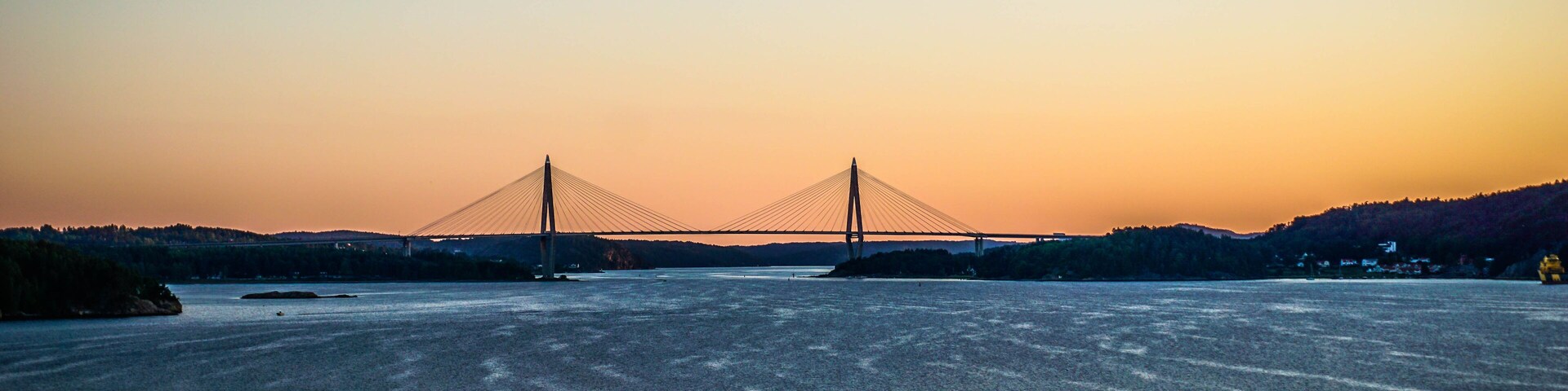 A suspension bridge at sunset with a calm river in the foreground.