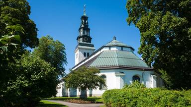 Köping church, white paint facade, copper-covered gable roof, Baroque style spire on copper-clad tower with clock, Old religious building surrounded by green garden, Sweden