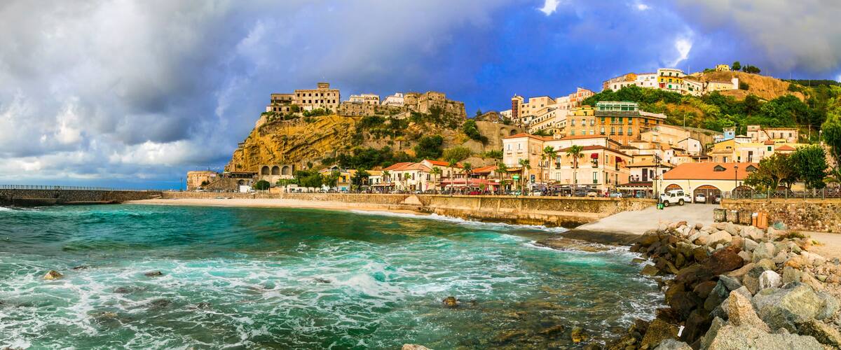 A coastal town with a historic castle on a hill, a beach, and rocky shoreline.