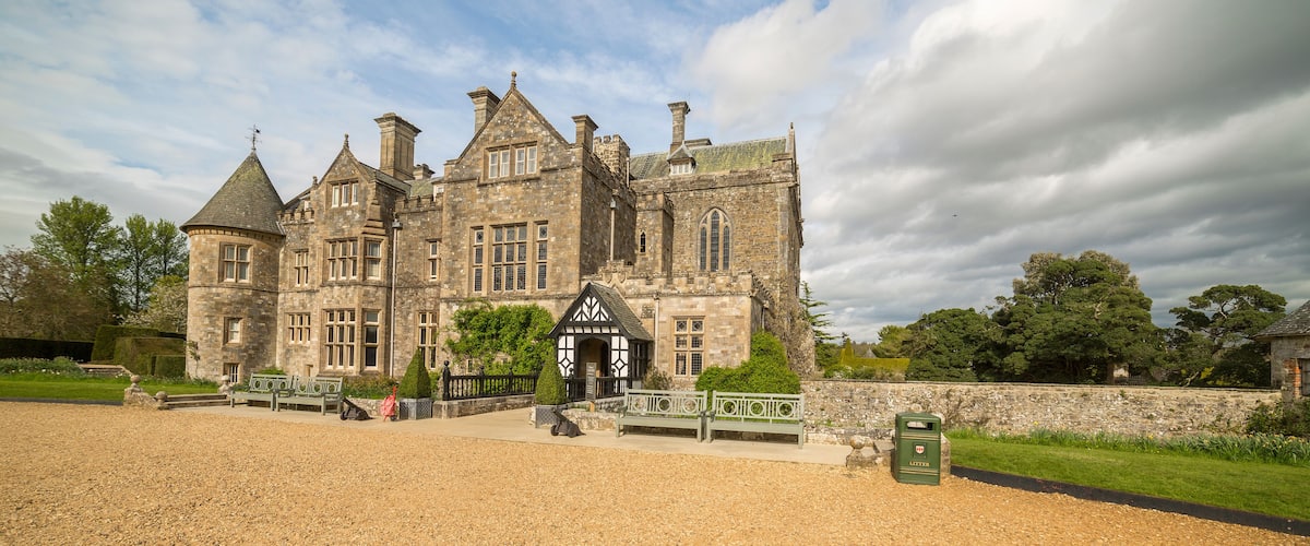 A large stone building with a traditional architectural style, featuring multiple chimneys and a prominent entrance with a small porch.