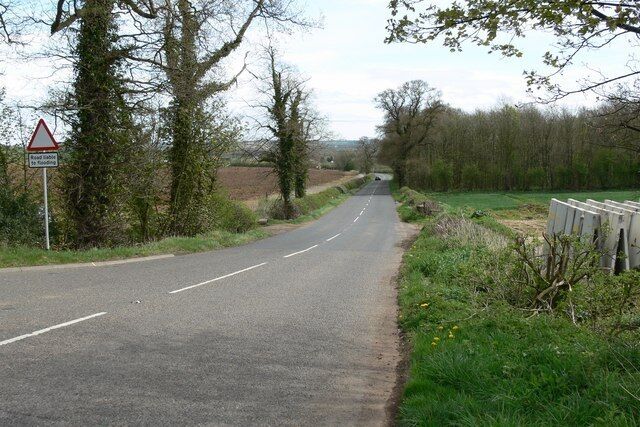 A rural road with a warning sign, surrounded by trees and fields.
