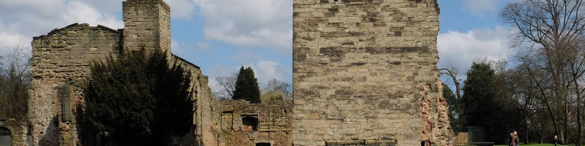 A medieval stone tower with battlements, surrounded by grassy fields and trees under a partly cloudy sky.