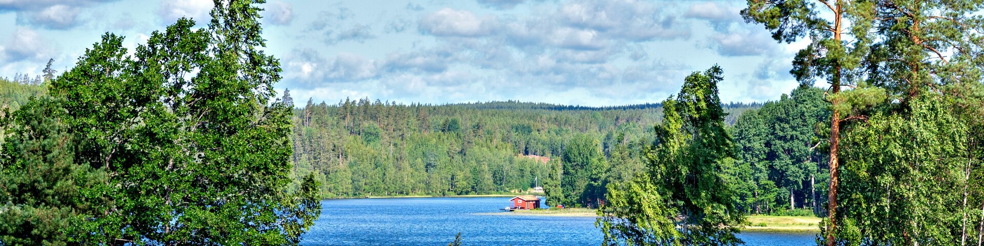 Un lago rodeado de bosques densos y una pequeña cabaña roja en la orilla.