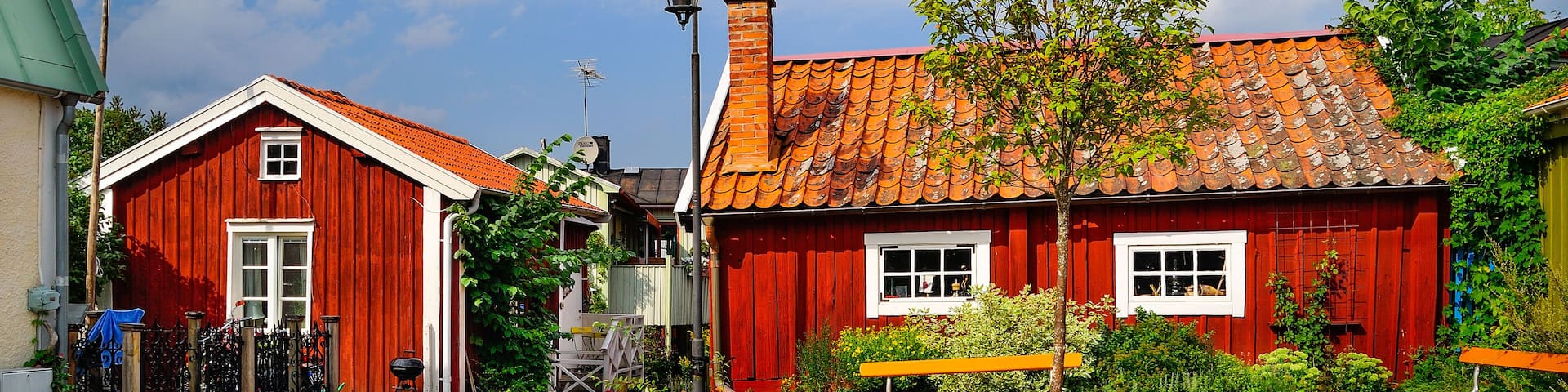 A cobblestone courtyard with red wooden houses, a bench, and a street lamp.