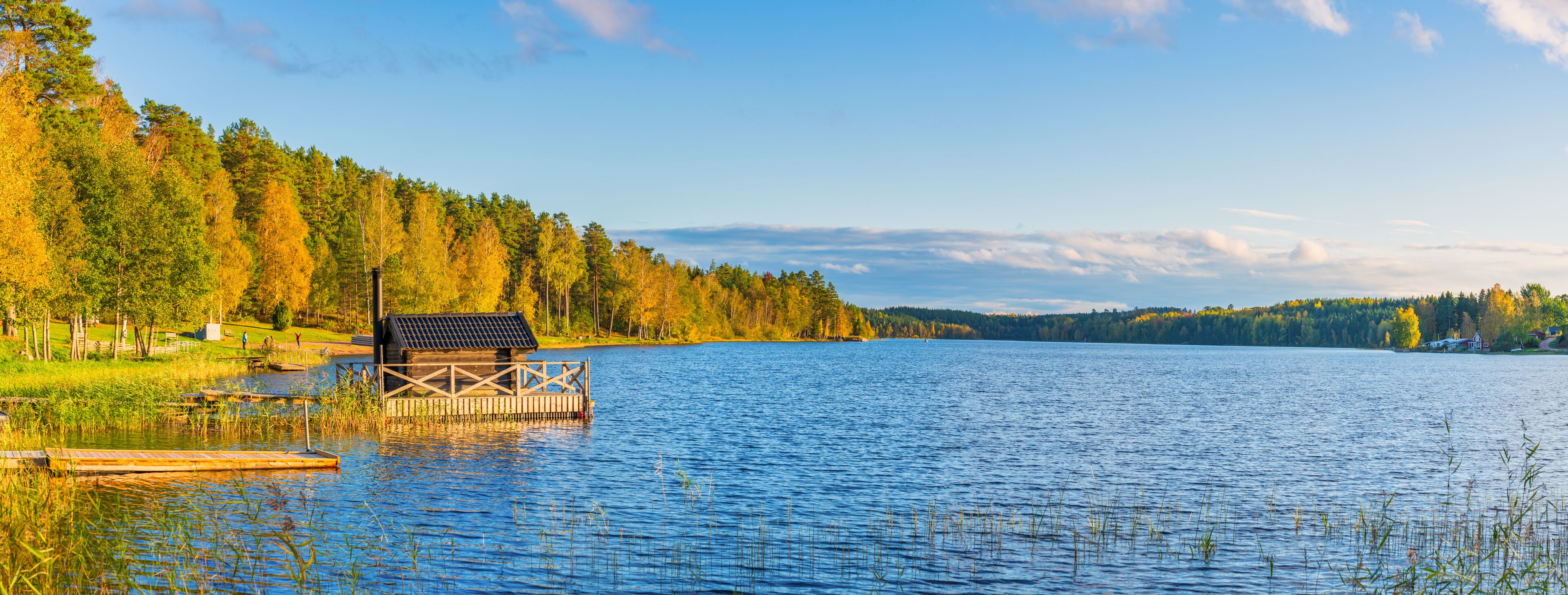 A wooden dock on a calm lake surrounded by autumn-colored trees.