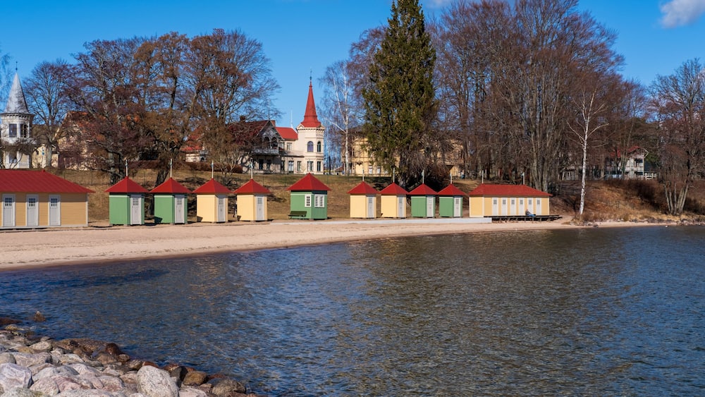 A lakeside with a row of colorful buildings, a church with a red roof, and a large tree.