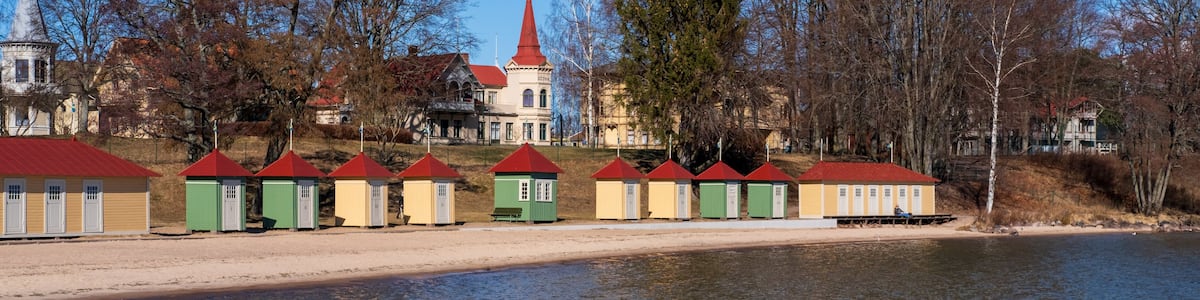 A lakeside with a row of colorful buildings, a church with a red roof, and a large tree.