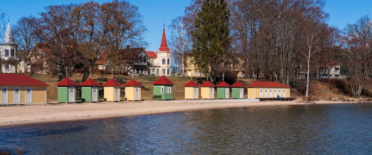 A lakeside with a row of colorful buildings, a church with a red roof, and a large tree.