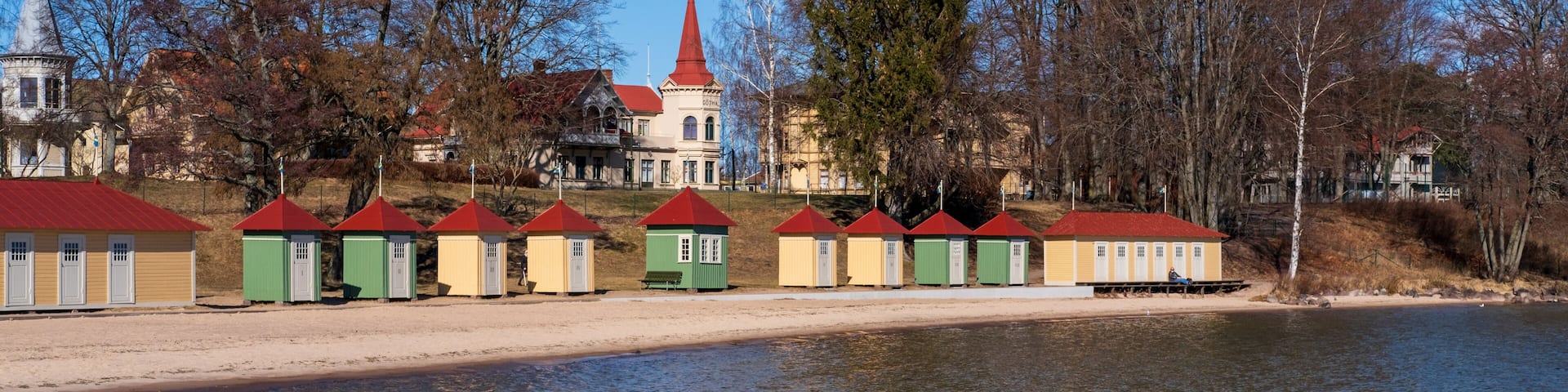 A lakeside with a row of colorful buildings, a church with a red roof, and a large tree.