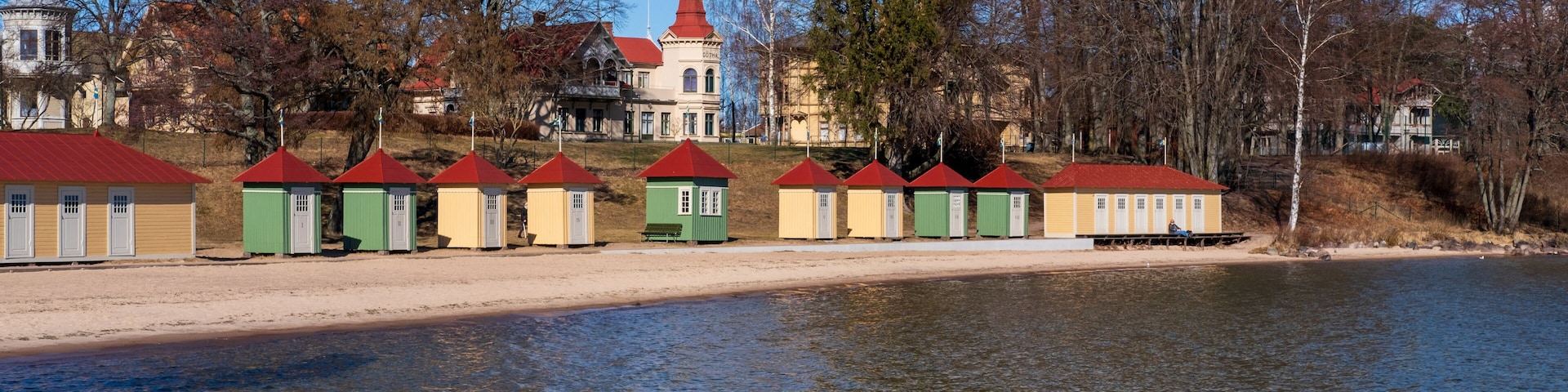 Un lago con una hilera de edificios coloridos, una iglesia de techo rojo y un árbol grande.