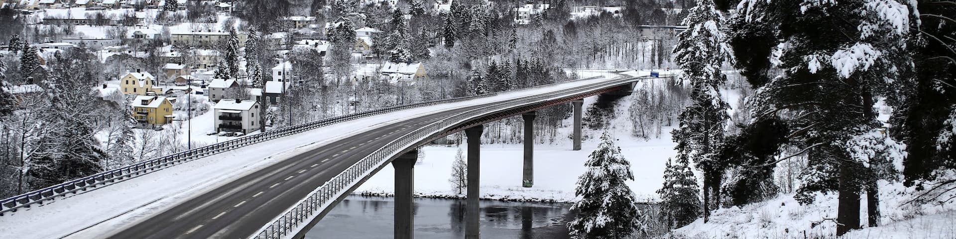 A snow-covered bridge over a river with a town in the background.