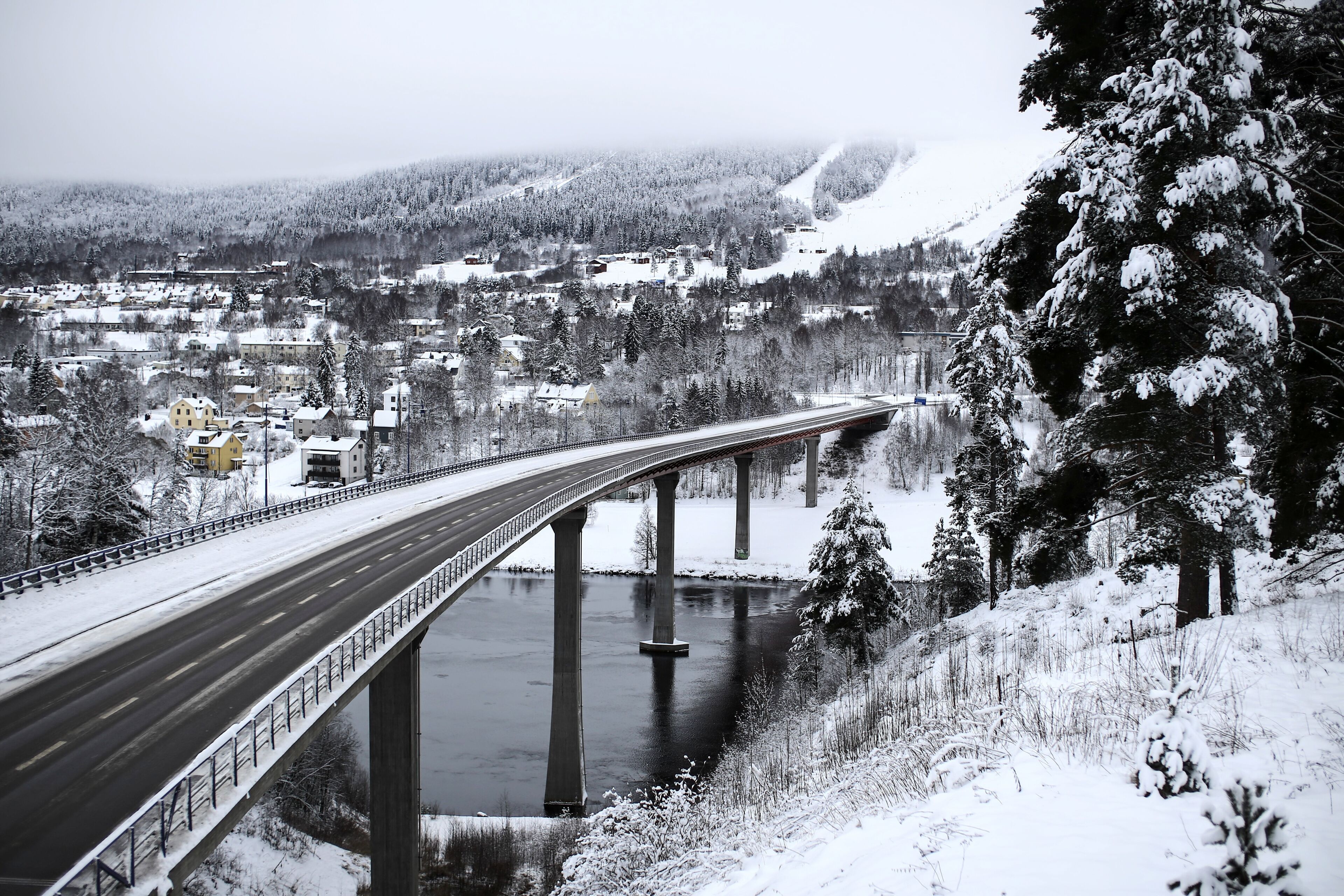 A snow-covered bridge over a river with a town in the background.