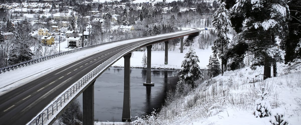 A snow-covered bridge over a river with a town in the background.