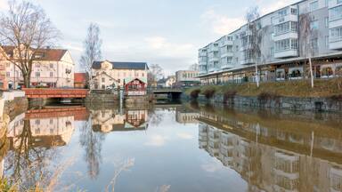 Une rivière paisible où se reflètent des bâtiments, un pont rouge et un mur de pierre.