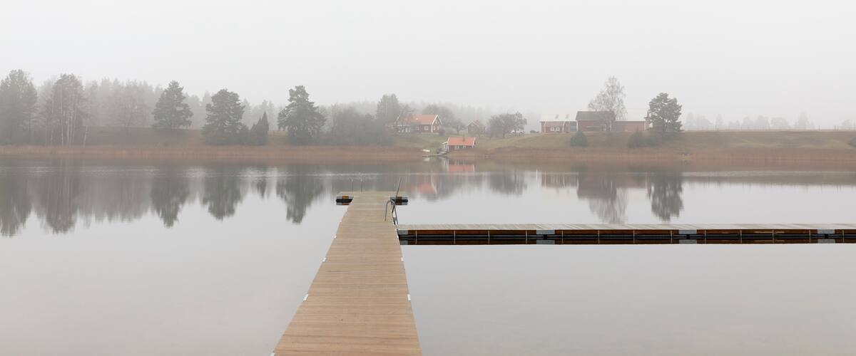 A wooden pier extending into a calm lake with reflections of trees and houses in the background.
