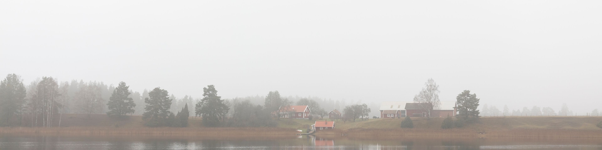 A wooden pier extending into a calm lake with reflections of trees and houses in the background.