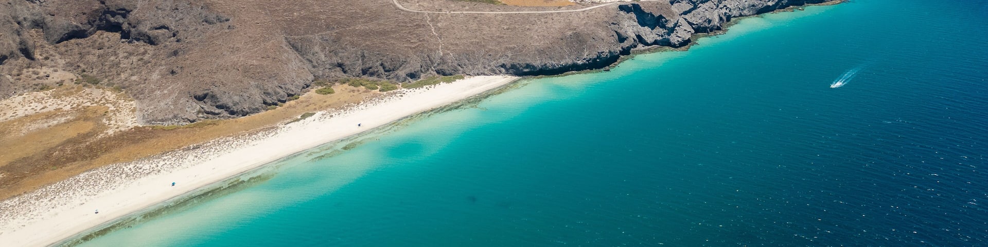 A coastal landscape with a beach, clear turquoise waters, and a mountainous backdrop.