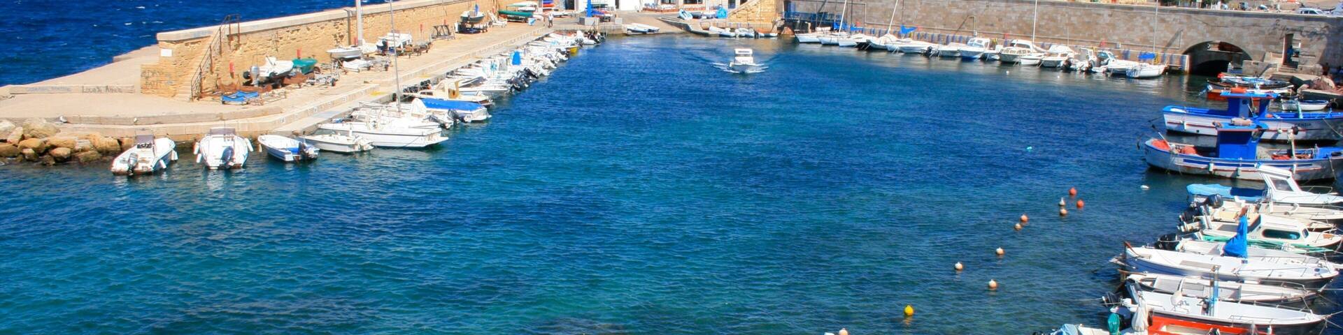 A harbor with numerous boats docked along the piers, a sandy beach, and a stone wall.