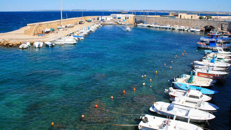 A harbor with numerous boats docked along the piers, a sandy beach, and a stone wall.