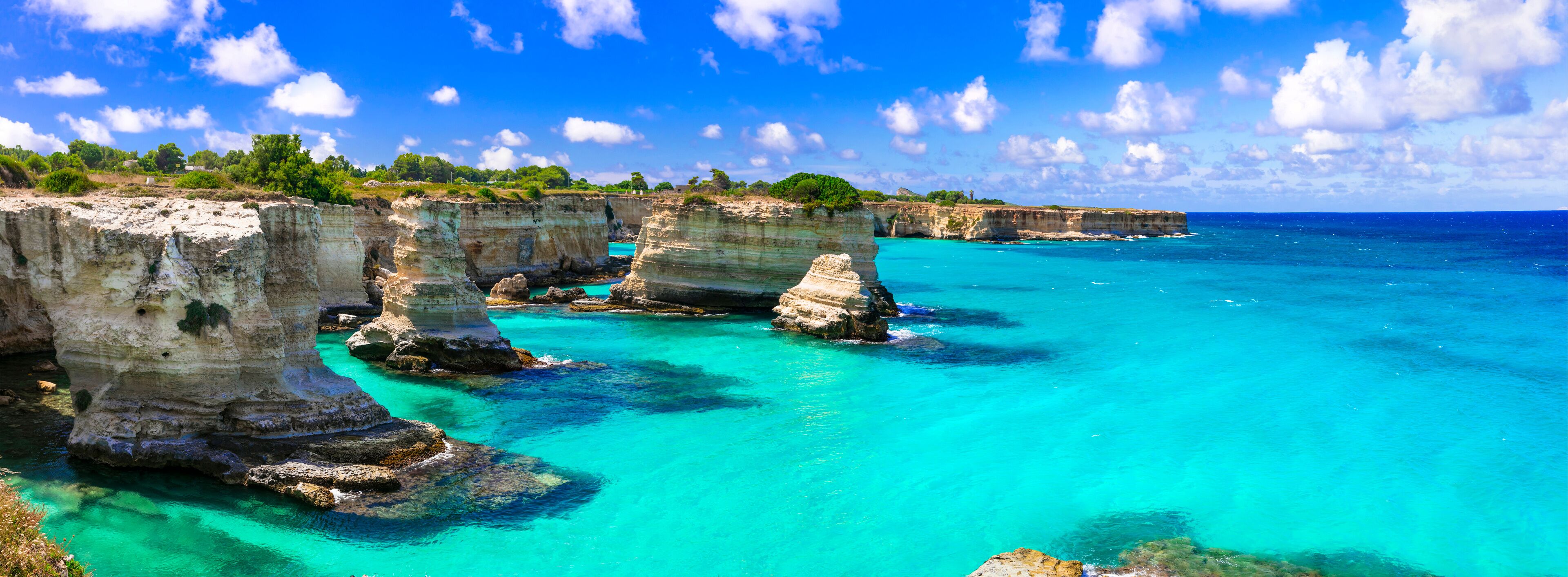 A coastal landscape with prominent limestone cliffs and clear turquoise waters.