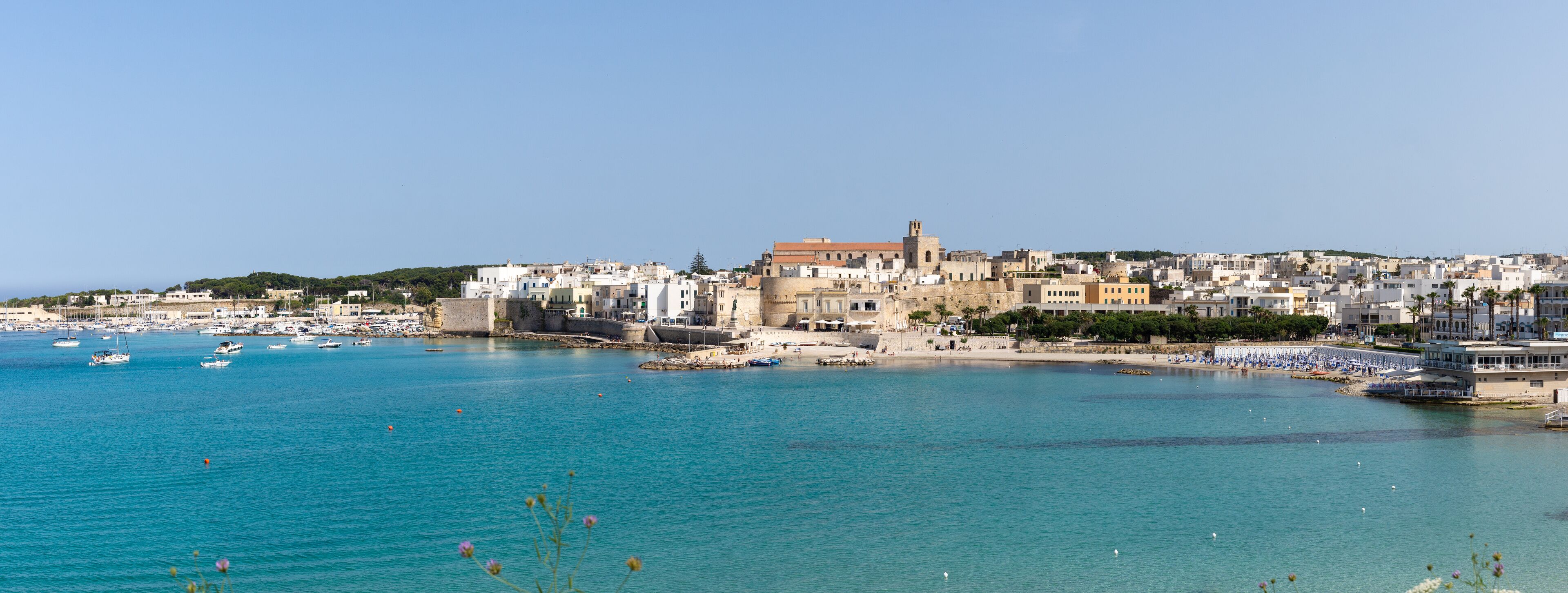 A coastal town with a historic castle, boats, and a clear blue sea.