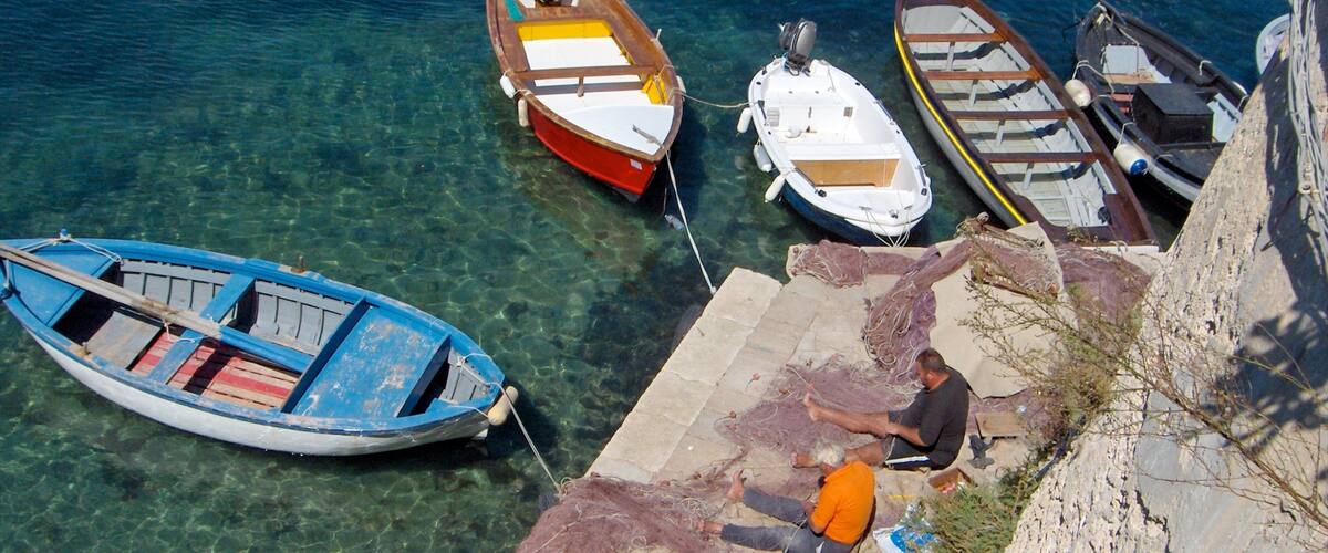 A clear blue sea with several boats docked at a pier.