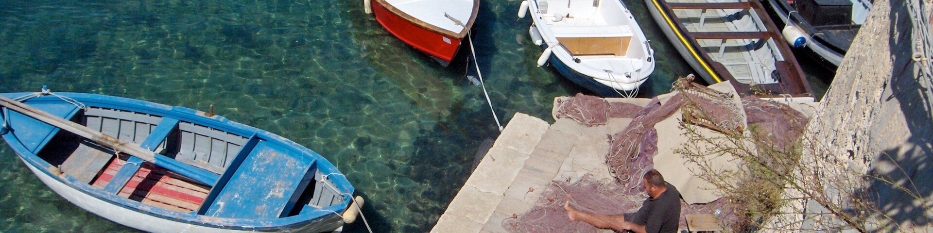 A clear blue sea with several boats docked at a pier.