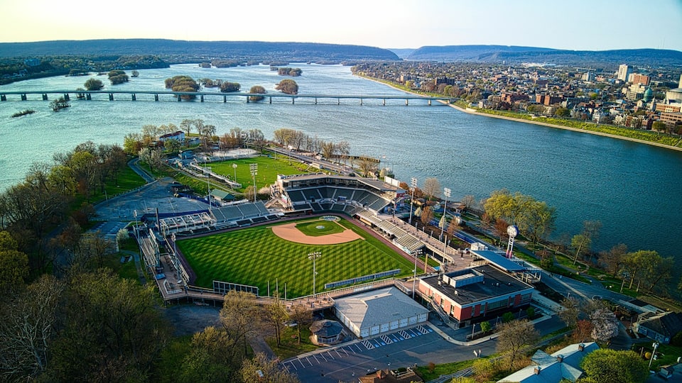 An aerial view of a baseball stadium with a river and bridge in the background.
