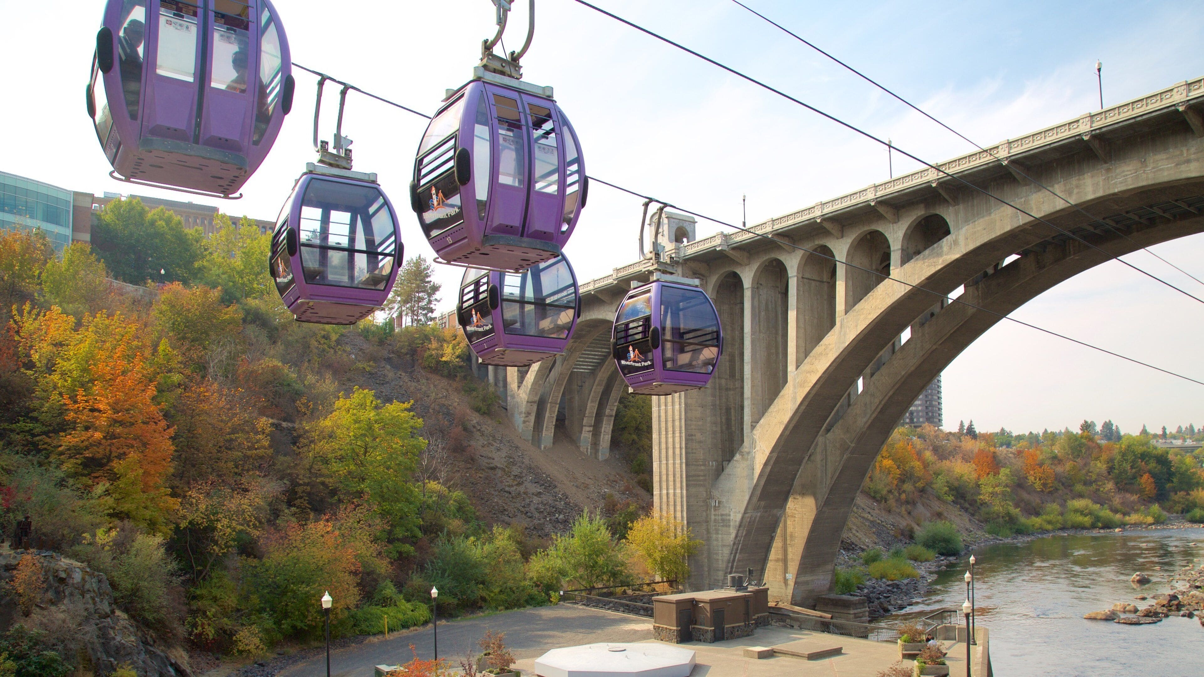 A cable car system over a bridge with autumn foliage and a river below.