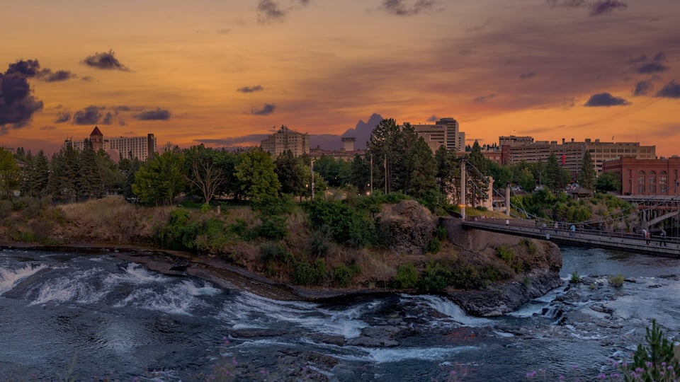 A river flowing through a city with a bridge and a sunset sky.