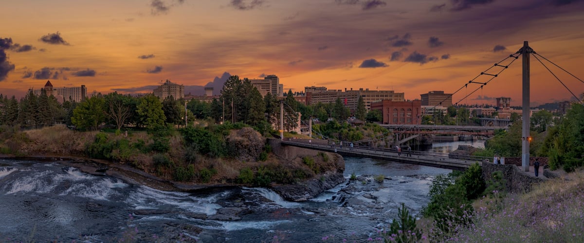 A river flowing through a city with a bridge and a sunset sky.