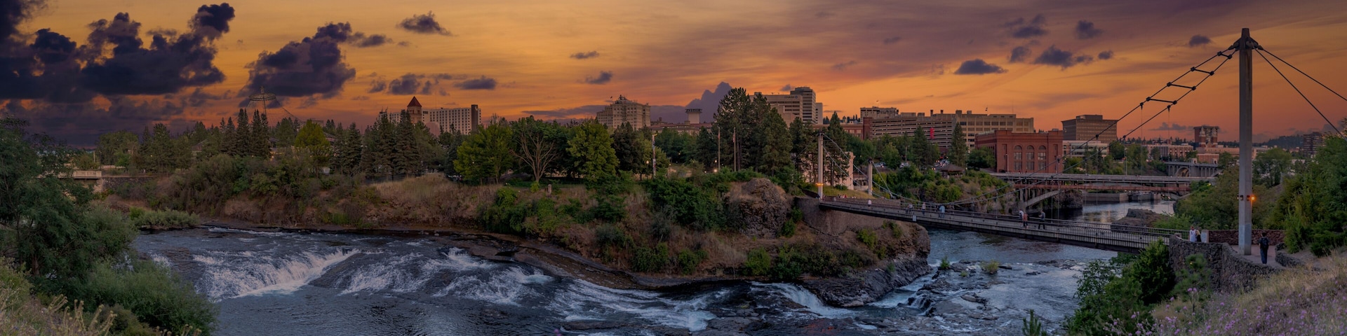 A river flowing through a city with a bridge and a sunset sky.