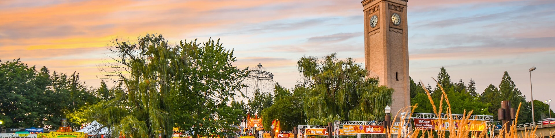A clock tower, a bridge, a Ferris wheel, and a body of water at sunset.