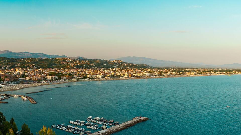 A coastal city with a marina, mountains in the background, and a clear sky.
