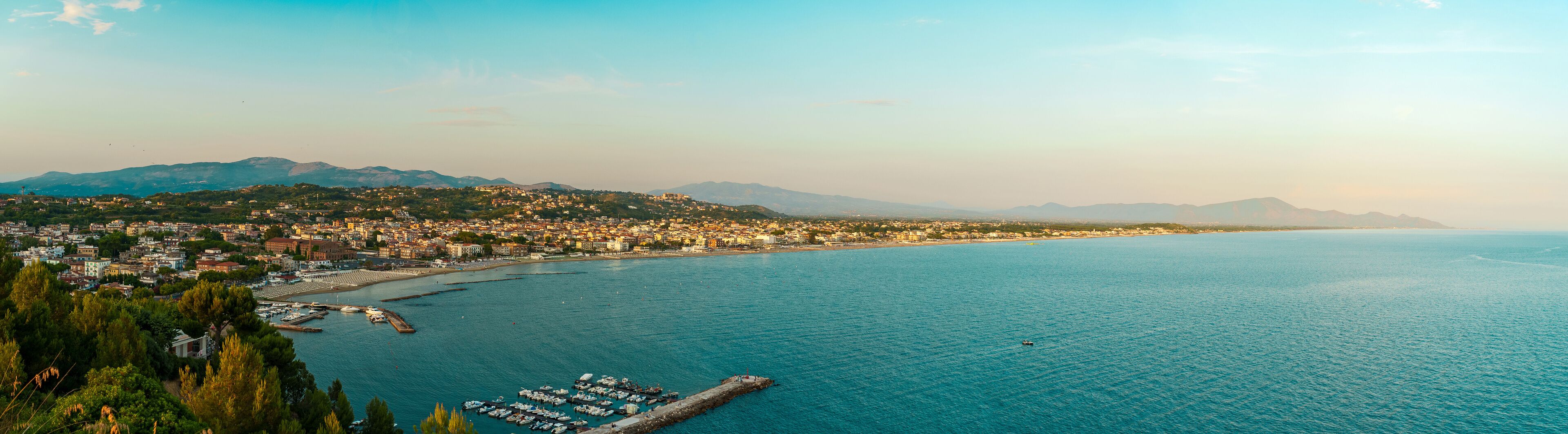 A coastal city with a marina, mountains in the background, and a clear sky.