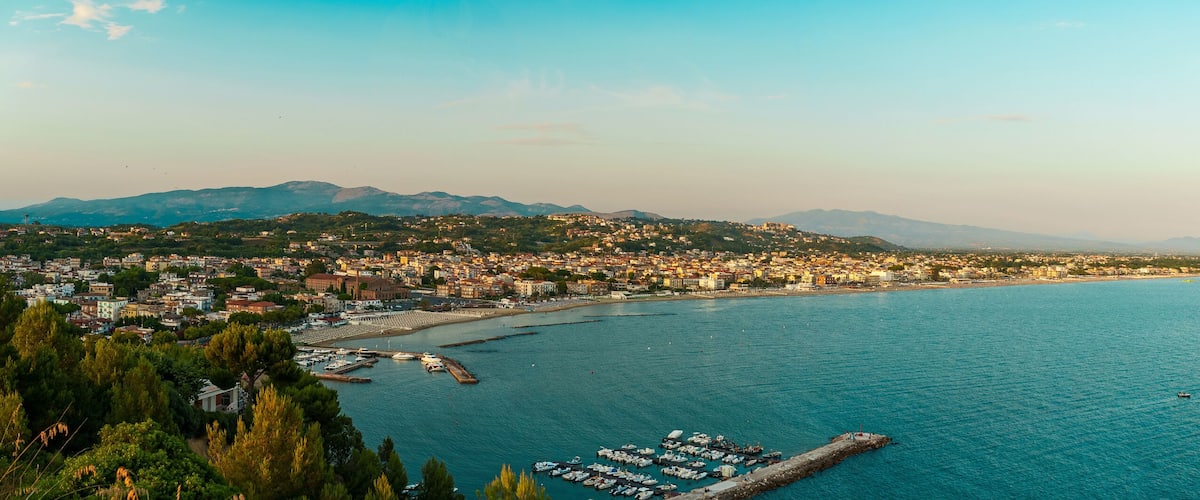 A coastal city with a marina, mountains in the background, and a clear sky.